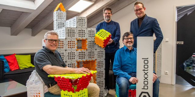 Vier Männer sitzen und stehen um Spielzeuggebäude herum.