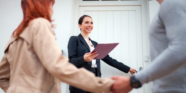 Herzliche Begrüßung einer Frau und eines Mannes durch eine Immobilienmaklerin an der Haustür.